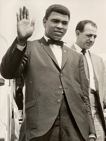 Vintage pressefoto af bokseren Muhammad Ali / Cassius Clay (1942 - 2016), der 
vinker ved ankomst til London Airport til kampen mod Henry Cooper i 1966