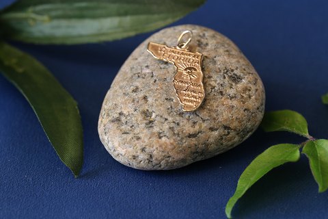 Pendant/charm in 14 carat gold. The pendant is shaped like Florida, and engraved 
with writing.